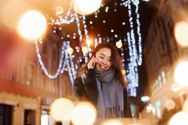 Telefonla konuşuyor. Şehirdeki sevimli ve mutlu Asyalı genç bayan yeni yılı kutluyor..
