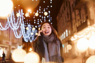 Telefonla konuşuyor. Şehirdeki sevimli ve mutlu Asyalı genç bayan yeni yılı kutluyor..