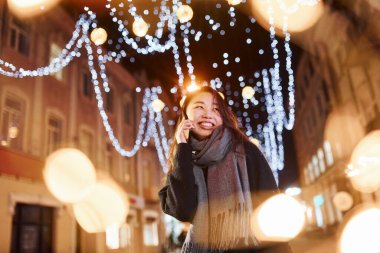 Telefonla konuşuyor. Şehirdeki sevimli ve mutlu Asyalı genç bayan yeni yılı kutluyor..