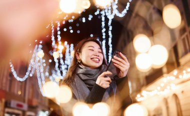 Telefon kullanıyor. Şehirdeki sevimli ve mutlu Asyalı genç bayan yeni yılı kutluyor..