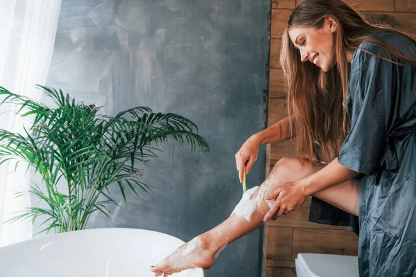 Güzel genç bayanın evde banyoda boş zamanı var. Bacaklarını tıraş eder..