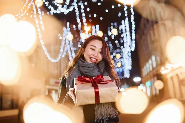 Hediye kutusuyla. Şehirdeki sevimli ve mutlu Asyalı genç bayan yeni yılı kutluyor..