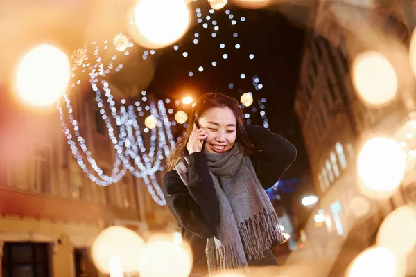 Telefonla konuşuyor. Şehirdeki sevimli ve mutlu Asyalı genç bayan yeni yılı kutluyor..