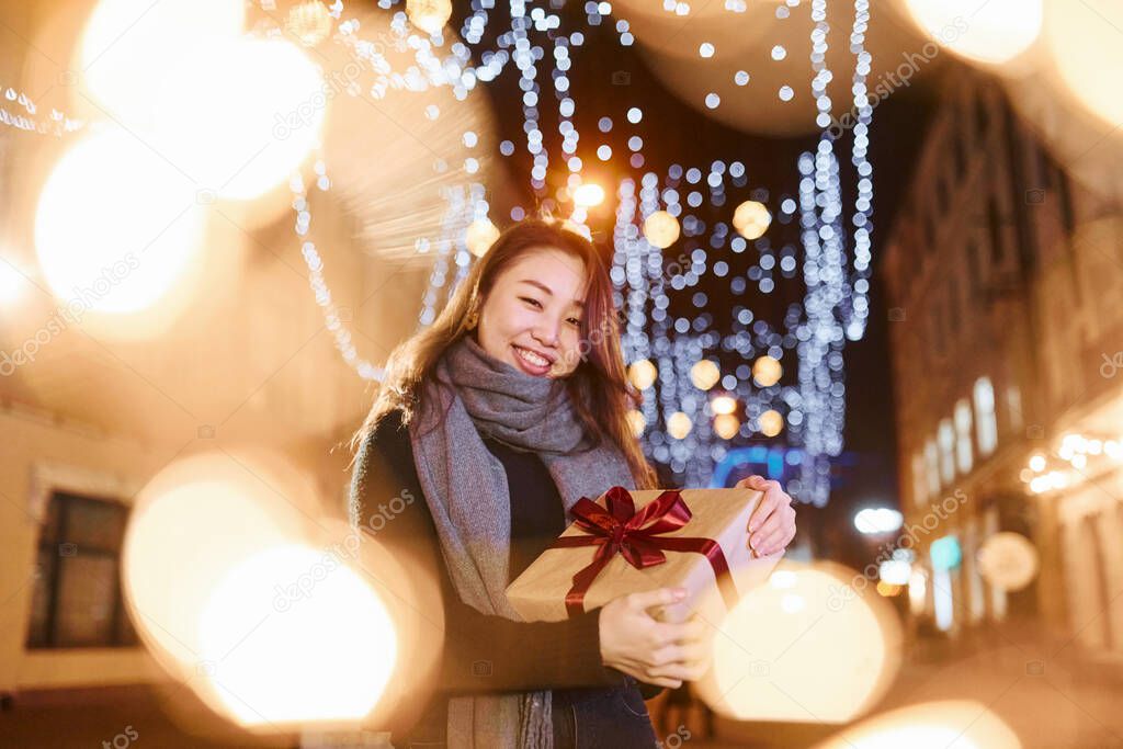 With gift box. Cute and happy asian young woman outdoors in the city celebrates New year.