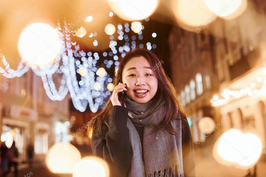 Talks by phone. Cute and happy asian young woman outdoors in the city celebrates New year.