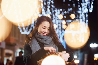 Hediye kutusuyla. Şehirdeki sevimli ve mutlu Asyalı genç bayan yeni yılı kutluyor..