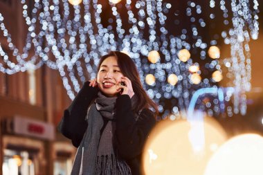 Telefonla konuşuyor. Şehirdeki sevimli ve mutlu Asyalı genç bayan yeni yılı kutluyor..