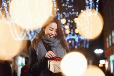 Hediye kutusuyla. Şehirdeki sevimli ve mutlu Asyalı genç bayan yeni yılı kutluyor..