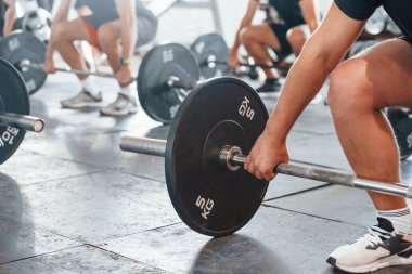 By using heavy weights. Group of young sportive people have crossfit day indoors in gym.