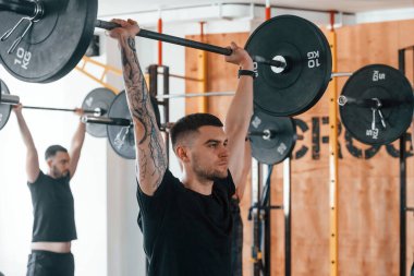 Halteri kaldırıyorum. Bir grup genç sporcu spor salonunda iç içe geçiyor..