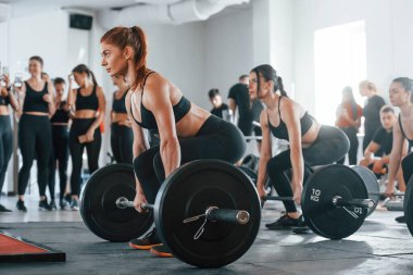 Halteri kaldırıyorum. Bir grup genç sporcu spor salonunda iç içe geçiyor..