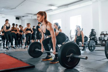 Halteri kaldırıyorum. Bir grup genç sporcu spor salonunda iç içe geçiyor..