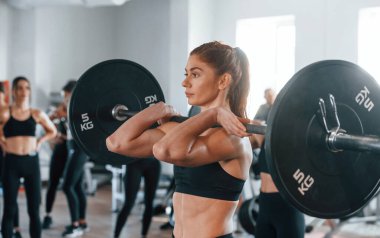 Halteri kaldırıyorum. Bir grup genç sporcu spor salonunda iç içe geçiyor..