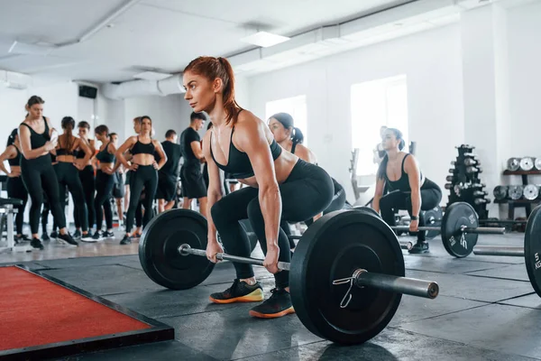 Halteri kaldırıyorum. Bir grup genç sporcu spor salonunda iç içe geçiyor..