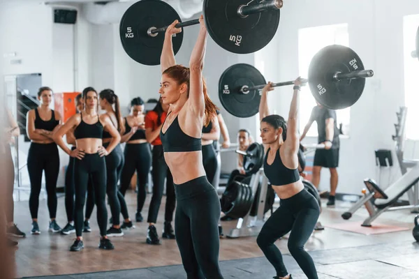Halteri kaldırıyorum. Bir grup genç sporcu spor salonunda iç içe geçiyor..