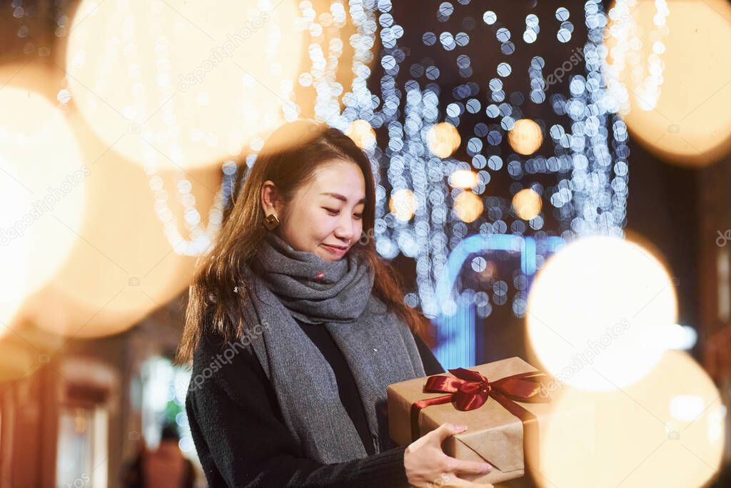With gift box. Cute and happy asian young woman outdoors in the city celebrates New year.