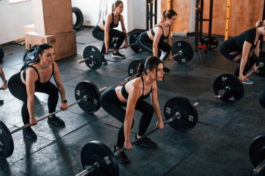 Halterli çömelmeler. Bir grup genç sporcu spor salonunda iç içe geçiyor..