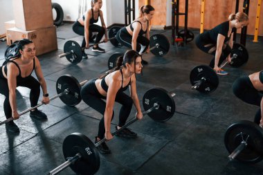 Halterli çömelmeler. Bir grup genç sporcu spor salonunda iç içe geçiyor..