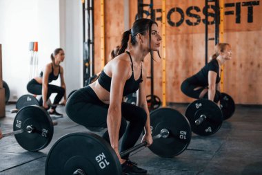 Halterli çömelmeler. Bir grup genç sporcu spor salonunda iç içe geçiyor..