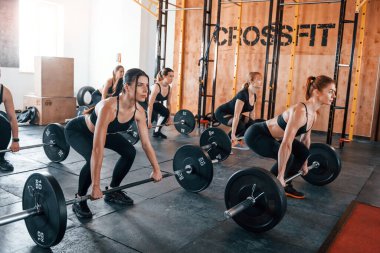 Halterli çömelmeler. Bir grup genç sporcu spor salonunda iç içe geçiyor..