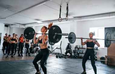 Halterli çömelmeler. Bir grup genç sporcu spor salonunda iç içe geçiyor..