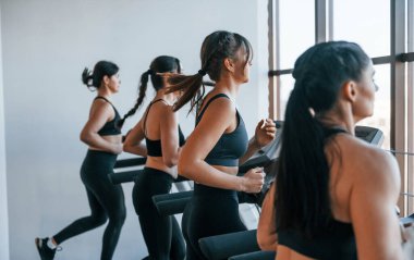 Koşu bandında koşmak. Bir grup genç sporcu spor salonunda iç içe geçiyor..