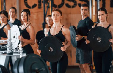 Ağırlık tutuyor. Bir grup genç sporcu spor salonunda iç içe geçiyor..