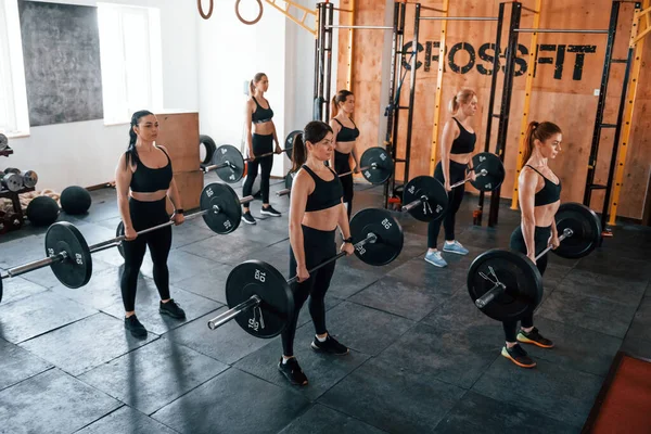 Halterli çömelmeler. Bir grup genç sporcu spor salonunda iç içe geçiyor..