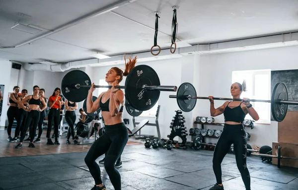 Halterli çömelmeler. Bir grup genç sporcu spor salonunda iç içe geçiyor..
