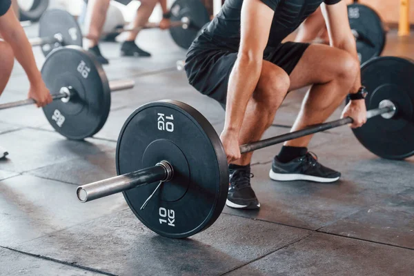 By using heavy weights. Group of young sportive people have crossfit day indoors in gym.