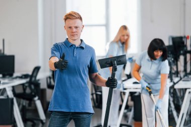 Guy with vacuum cleaner. Group of workers clean modern office together at daytime.