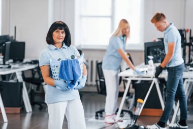 Woman with basket. Group of workers clean modern office together at daytime.