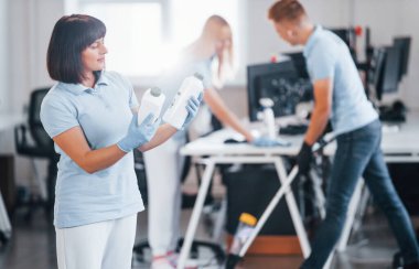 Group of workers clean modern office together at daytime.