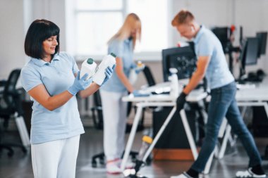Group of workers clean modern office together at daytime.