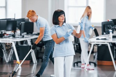 Group of workers clean modern office together at daytime.