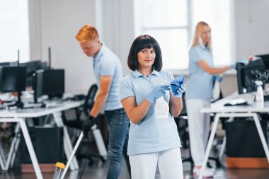Group of workers clean modern office together at daytime.