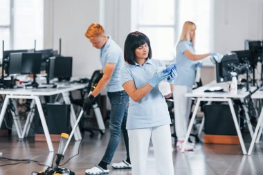 Cleans floor. Group of workers clean modern office together at daytime.