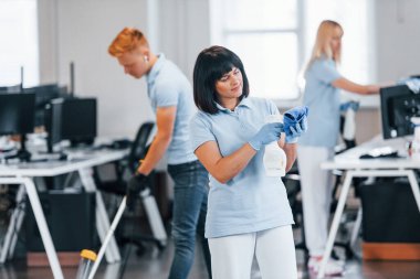 Cleans floor. Group of workers clean modern office together at daytime.