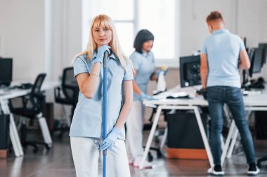 Cleans floor. Group of workers clean modern office together at daytime.