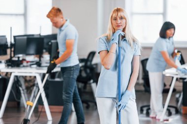 Cleans floor. Group of workers clean modern office together at daytime.