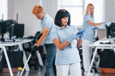Cleans floor. Group of workers clean modern office together at daytime.
