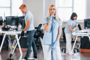 Cleans floor. Group of workers clean modern office together at daytime.