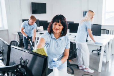 Group of workers clean modern office together at daytime.
