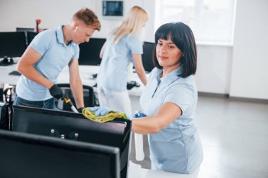 Cleans monitor. Group of workers clean modern office together at daytime.