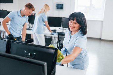 Cleans monitor. Group of workers clean modern office together at daytime.