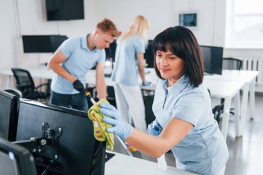 Cleans monitor. Group of workers clean modern office together at daytime.