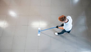 Mavi gömlekli ve elektrikli süpürge kullanan koruyucu eldivenli adam..