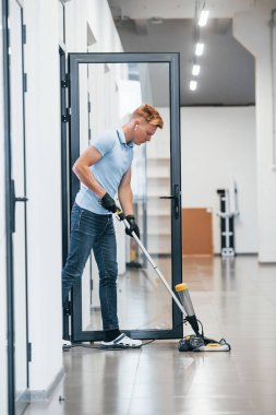 Genç adam modern ofiste çalışıyor. Elektrik süpürgesi kullanıyor.