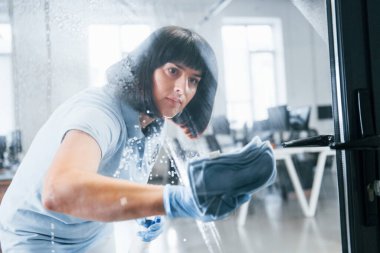 Kadın kirli pencereyi havluyla temizliyor. Camdan bak..