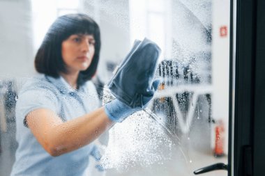 Kadın kirli pencereyi havluyla temizliyor. Camdan bak..